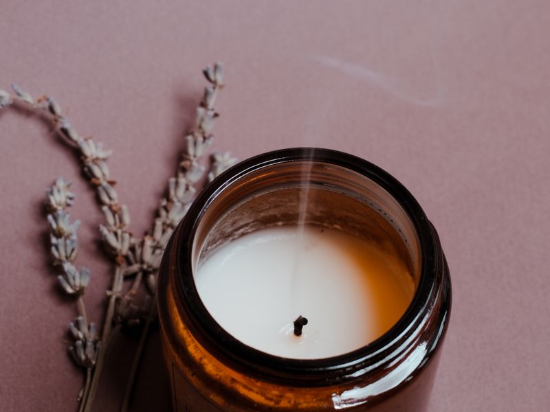 Lit soy candle in an amber jar next to dried lavender on a pink surface